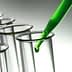 Green liquid being dropped into a glass test tube with a pipette. - Olive Oil Times
