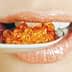 Close-up of a person's mouth holding a spoon with orange caviar beads. - Olive Oil Times
