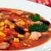 Bowl of chicken and vegetable soup with corn, beans, and herbs on a white plate. - Olive Oil Times
