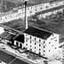 Black and white image of the Salov olive oil factory building with a tall chimney. - Olive Oil Times