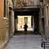 Individual walking through a narrow alleyway with brick walls and a cat following. - Olive Oil Times