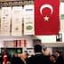 Turkish flag with a white star and crescent displayed at an indoor event with attendees. - Olive Oil Times