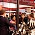 Group of people engaging in conversation at a wine tasting event with bottles displayed. - Olive Oil Times