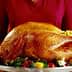 A person holding a large roasted turkey on a silver serving platter with garnishes. - Olive Oil Times
