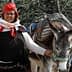 A woman in traditional attire standing next to a donkey with a saddle and bags. - Olive Oil Times