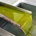 Stream of green olive oil flowing from a stainless steel spout into a perforated container. - Olive Oil Times