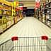 View of a supermarket aisle with shelves stocked with various products and a shopping cart in the foreground. - Olive Oil Times