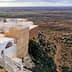 Aerial view of a landscape in Tunisia featuring olive groves and a building on a cliff edge. - Olive Oil Times