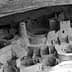 Black and white image of an ancient cliff dwelling with circular and rectangular structures. - Olive Oil Times
