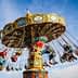 Colorful swing ride with multiple seats and riders at an amusement park against a blue sky. - Olive Oil Times
