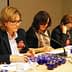 Three women seated at a conference table with blue tasting cups in front of them, engaged in discussion. - Olive Oil Times