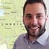 Man with a beard smiling in front of a map of Umbria, Italy, showing various towns and geographical features. - Olive Oil Times