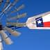 Close-up of a windmill with a Texas state flag attached to its arm against a blue sky. - Olive Oil Times