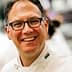 Chef wearing a white uniform and glasses, smiling at the camera in a kitchen setting. - Olive Oil Times