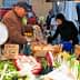 A market vendor handling fresh vegetables and fruits at a market stall with a customer selecting items. - Olive Oil Times
