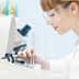 Female scientist in a lab coat and safety glasses operating laboratory equipment with test tubes. - Olive Oil Times