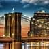 Brooklyn Bridge with illuminated towers and city skyline during sunset. - Olive Oil Times