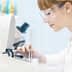 Laboratory technician wearing safety glasses examining a sample under a microscope. - Olive Oil Times