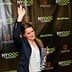 Woman with long hair raising her hand while holding an award at a culinary event backdrop. - Olive Oil Times
