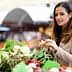 Woman examining fresh vegetables at a market stall with various produce visible. - Olive Oil Times