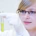Woman wearing glasses and a lab coat holding a test tube with yellow liquid in a laboratory setting. - Olive Oil Times