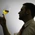 Silhouette of a person holding a glass of yellow liquid, examining it with a thoughtful expression. - Olive Oil Times