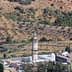 A tall minaret located in a rural area with olive trees in the background. - Olive Oil Times