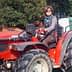 A woman wearing sunglasses and a striped shirt sitting on a red tractor, holding a tool. - Olive Oil Times
