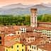 Aerial view of Lucca's rooftops featuring a historic tower and surrounding mountains. - Olive Oil Times