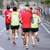 Three runners wearing colorful athletic clothing jogging on a road during a running event. - Olive Oil Times