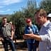 A group of people gathered in an olive grove, with one person speaking to the others. - Olive Oil Times