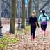 Two women jogging on a path lined with trees in a park during autumn. - Olive Oil Times