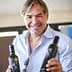 A man smiling while holding two bottles of olive oil in each hand. - Olive Oil Times