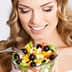Woman with long blonde hair smiling while holding a bowl of colorful salad with vegetables and olives. - Olive Oil Times