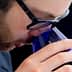 Individual wearing glasses bringing a blue glass close to their face for smelling. - Olive Oil Times