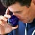 Man holding a blue glass cup and smelling the contents while tasting olive oil. - Olive Oil Times