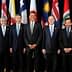 Group of ten political leaders posing for a photo at an international summit with flags in the background. - Olive Oil Times