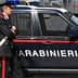 A Carabinieri officer standing next to a marked police vehicle in an urban setting. - Olive Oil Times