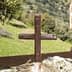 A wooden cross placed on a rock in a natural outdoor setting with greenery in the background. - Olive Oil Times