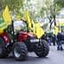Red tractor surrounded by yellow flags at a demonstration in an urban area. - Olive Oil Times