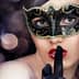 Woman with a black masquerade mask and finger on lips, signaling silence. - Olive Oil Times