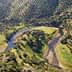 Aerial view of a winding river surrounded by olive trees in a hilly landscape. - Olive Oil Times