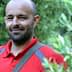 Man wearing a red polo shirt standing among olive trees with a slight smile. - Olive Oil Times