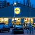 Exterior view of a Lidl supermarket with a lit sign and parked cars in front during dusk. - Olive Oil Times
