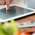 A person pointing at a tablet screen while preparing food in a kitchen setting. - Olive Oil Times