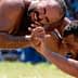 Two male wrestlers in a Greco-Roman wrestling match, grappling on a grassy field. - Olive Oil Times