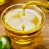 A glass bowl filled with olive oil with a stream pouring from a vessel and olives nearby. - Olive Oil Times