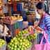 A woman selecting limes from a basket in a busy fruit market with people around her. - Olive Oil Times