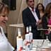 A woman smiling while serving olive oil at a tasting event with attendees in the background. - Olive Oil Times