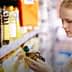 A woman inspecting a bottle of olive oil while shopping in a supermarket aisle. - Olive Oil Times